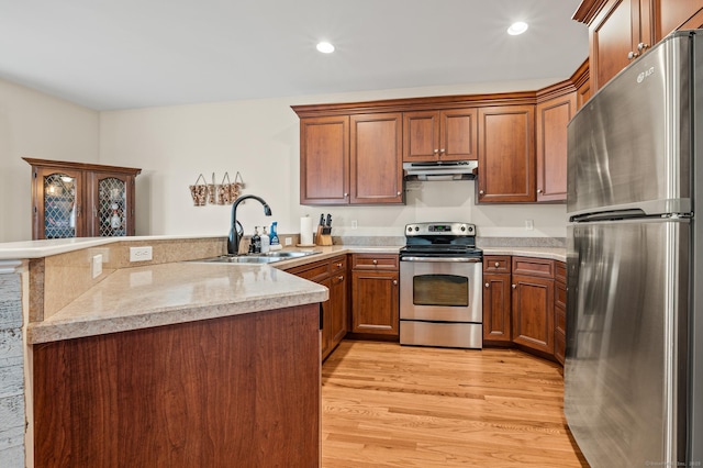 kitchen featuring light wood-style flooring, under cabinet range hood, a sink, appliances with stainless steel finishes, and a peninsula