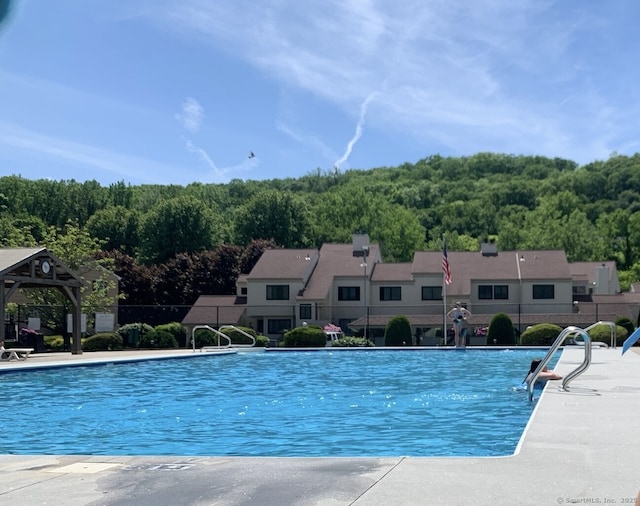 pool with a gazebo, a view of trees, a patio, and fence