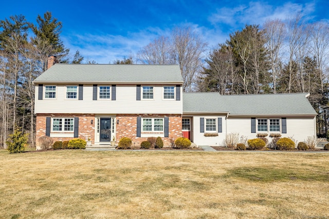 colonial home with brick siding, a chimney, a front lawn, and roof with shingles