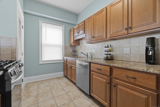 kitchen with a sink, light tile patterned flooring, light stone counters, baseboards, and appliances with stainless steel finishes
