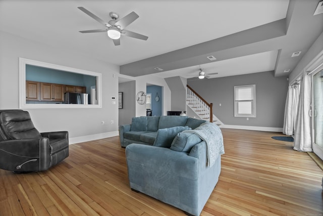 living room featuring stairway, baseboards, a ceiling fan, and light wood-style flooring