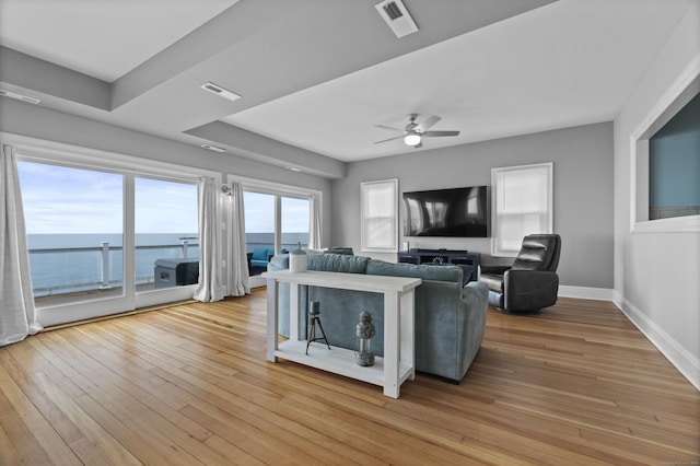 living area with visible vents, light wood-style flooring, baseboards, and ceiling fan