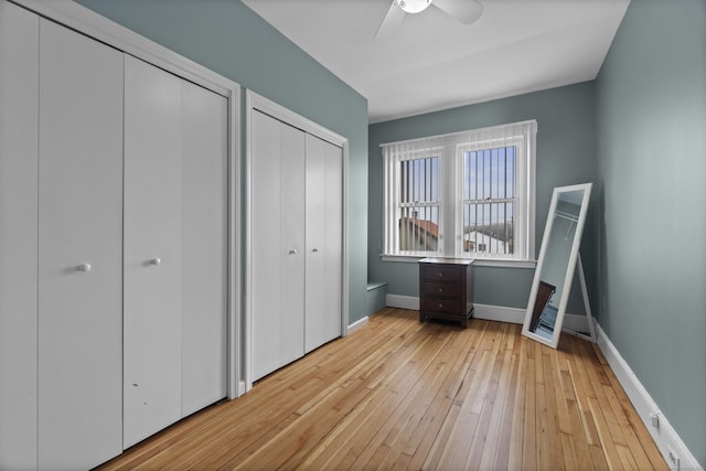 unfurnished bedroom featuring light wood-type flooring, ceiling fan, baseboards, and two closets