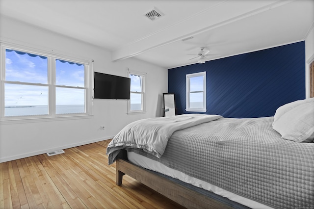 bedroom featuring baseboards, wood-type flooring, beam ceiling, and visible vents