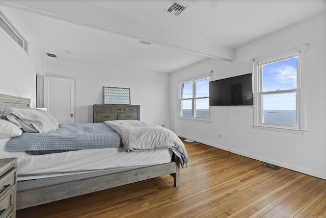 bedroom featuring light wood finished floors, beamed ceiling, baseboards, and visible vents