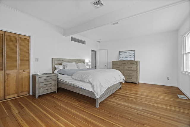 bedroom featuring baseboards, beamed ceiling, light wood-type flooring, and visible vents
