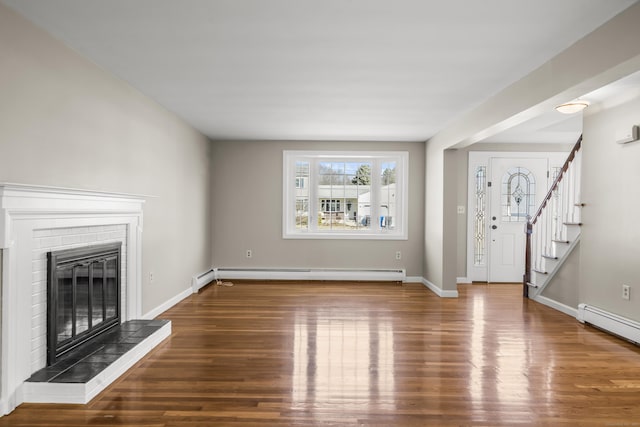 unfurnished living room featuring stairway, wood finished floors, baseboards, a brick fireplace, and baseboard heating