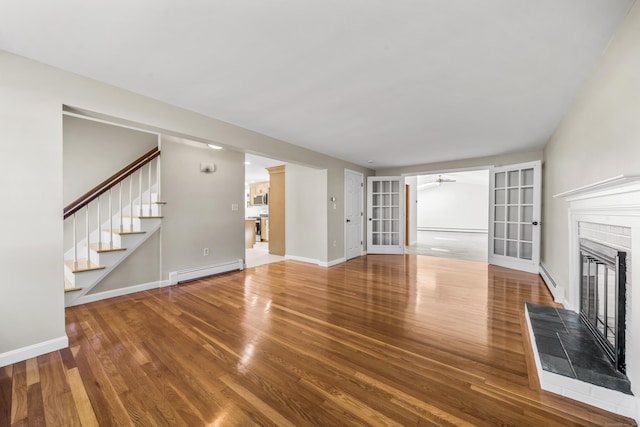 unfurnished living room featuring a glass covered fireplace, stairway, wood finished floors, and a baseboard radiator