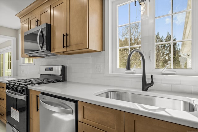 kitchen featuring brown cabinetry, a sink, light countertops, appliances with stainless steel finishes, and tasteful backsplash