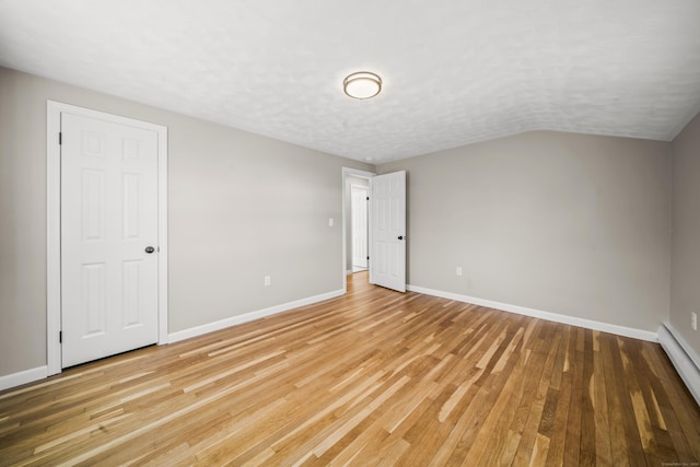 spare room with light wood-style flooring, a textured ceiling, a baseboard radiator, baseboards, and vaulted ceiling