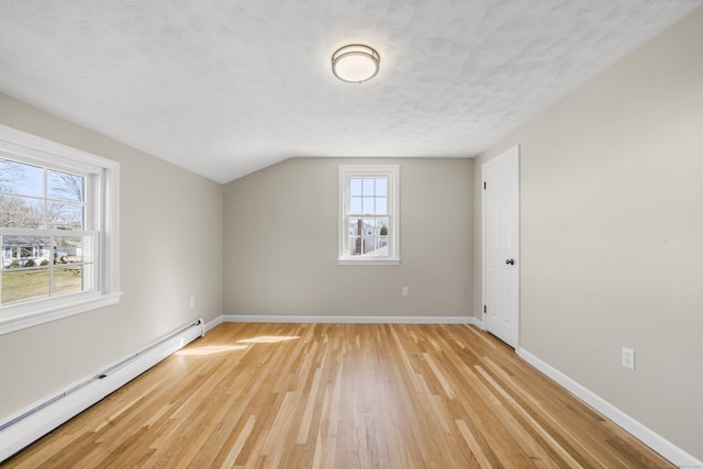 spare room featuring a textured ceiling, light wood-style floors, a baseboard radiator, baseboards, and vaulted ceiling