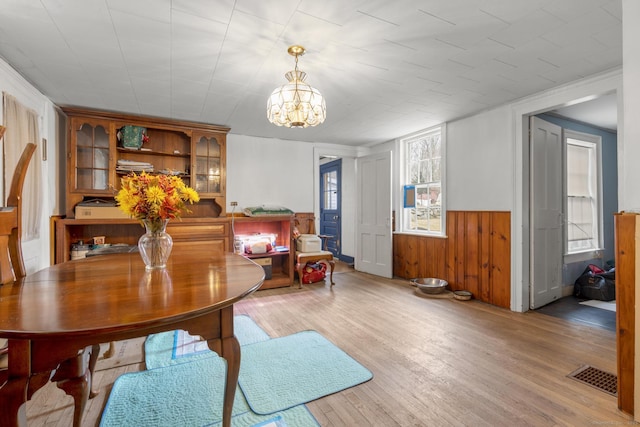 dining room with visible vents, wooden walls, a chandelier, a wainscoted wall, and light wood-style floors