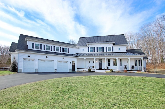 modern farmhouse featuring a front lawn, a standing seam roof, aphalt driveway, a porch, and a garage