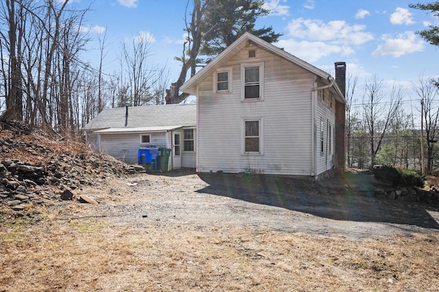 back of property with a chimney and dirt driveway