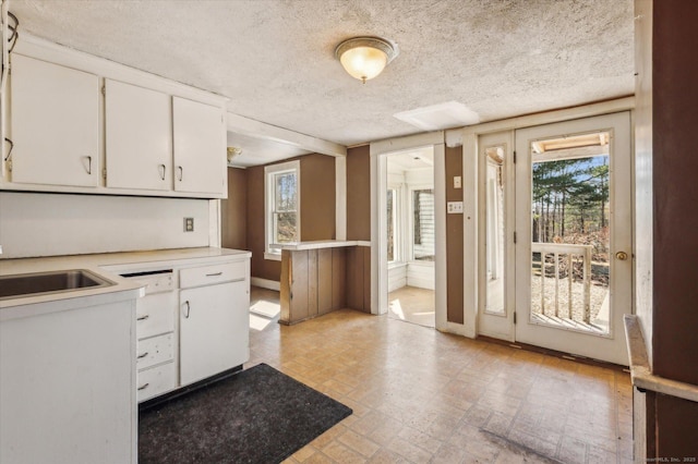 kitchen with a textured ceiling, a healthy amount of sunlight, light countertops, and white cabinetry