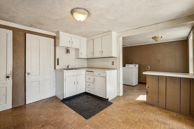 kitchen with washer / dryer, a sink, light countertops, white cabinets, and a textured ceiling