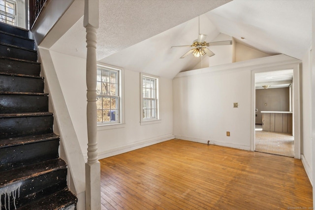 unfurnished living room with baseboards, lofted ceiling, ceiling fan, stairs, and wood-type flooring