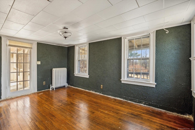 spare room with hardwood / wood-style floors, radiator heating unit, and a textured wall