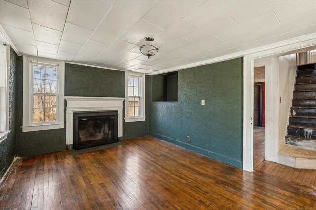 unfurnished living room with a wealth of natural light, stairway, a fireplace, and wood-type flooring