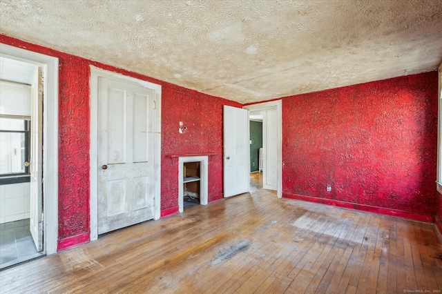 empty room featuring baseboards, a textured ceiling, a textured wall, and hardwood / wood-style floors