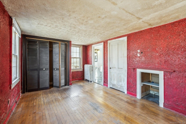 unfurnished bedroom featuring a textured ceiling, radiator heating unit, a textured wall, and hardwood / wood-style floors