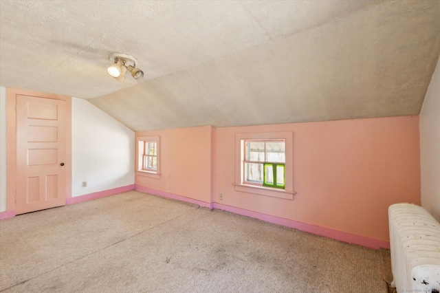 additional living space with radiator, a textured ceiling, lofted ceiling, and baseboards