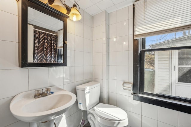 bathroom with a sink, toilet, and tile walls