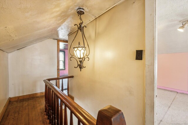 hallway with baseboards, lofted ceiling, wood-type flooring, a textured ceiling, and an upstairs landing