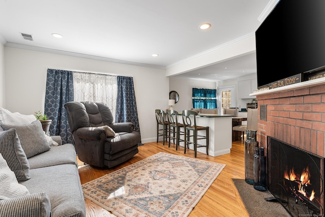 living room with visible vents, a brick fireplace, crown molding, recessed lighting, and light wood-style floors