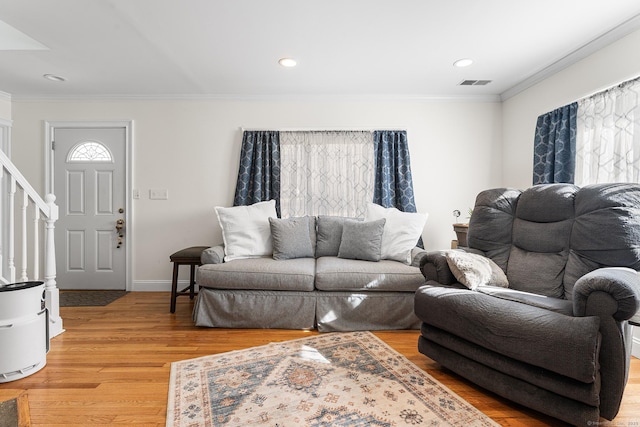 living area with visible vents, baseboards, stairway, ornamental molding, and light wood-style floors