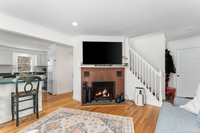 living area with stairway, ornamental molding, recessed lighting, a fireplace, and light wood-style floors