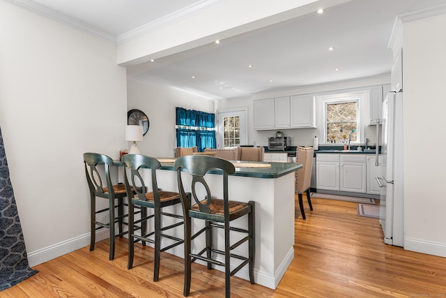 kitchen featuring light wood-style flooring, dark countertops, white cabinetry, a breakfast bar area, and crown molding