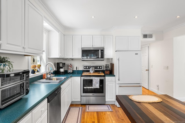 kitchen with dark countertops, visible vents, stainless steel appliances, white cabinetry, and a sink