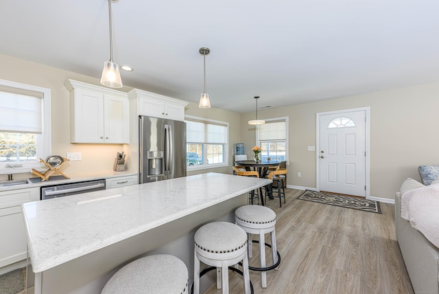 kitchen featuring a center island, white cabinetry, stainless steel appliances, light wood-style floors, and a breakfast bar area