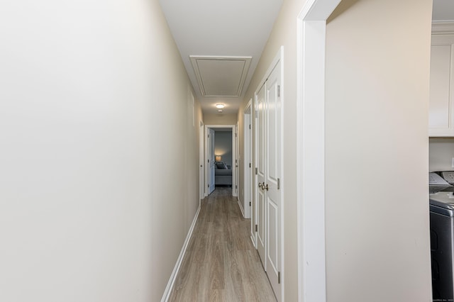 hallway featuring baseboards, attic access, and light wood-style flooring