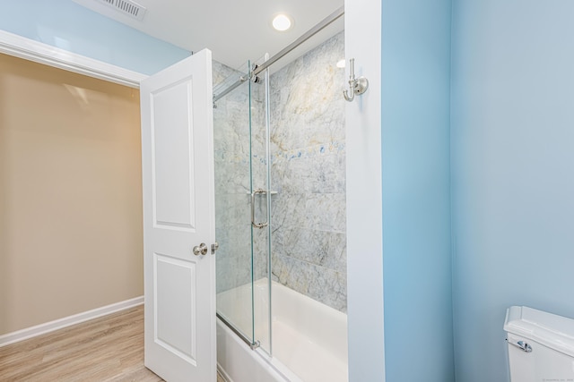 bathroom with wood finished floors, visible vents, baseboards, toilet, and combined bath / shower with glass door