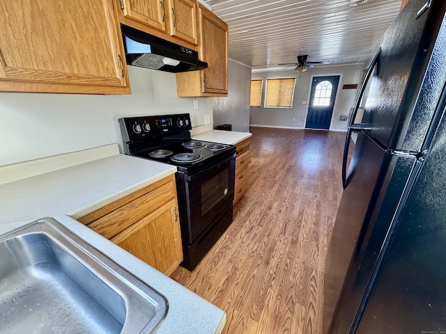 kitchen featuring black appliances, a ceiling fan, under cabinet range hood, wood finished floors, and light countertops