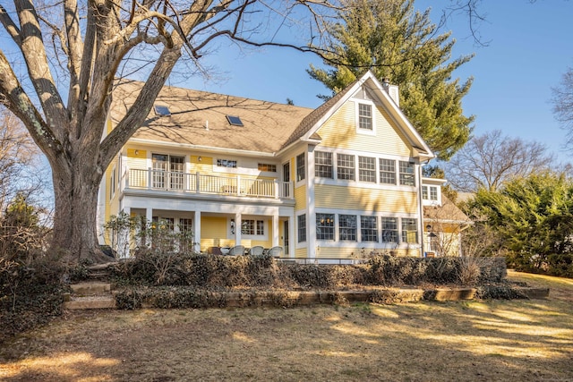 rear view of property featuring a balcony, a sunroom, and a chimney