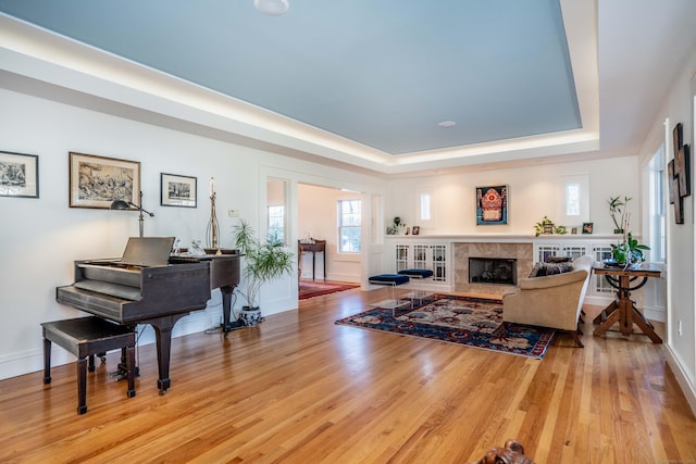 living area with a tray ceiling, baseboards, wood finished floors, and a fireplace