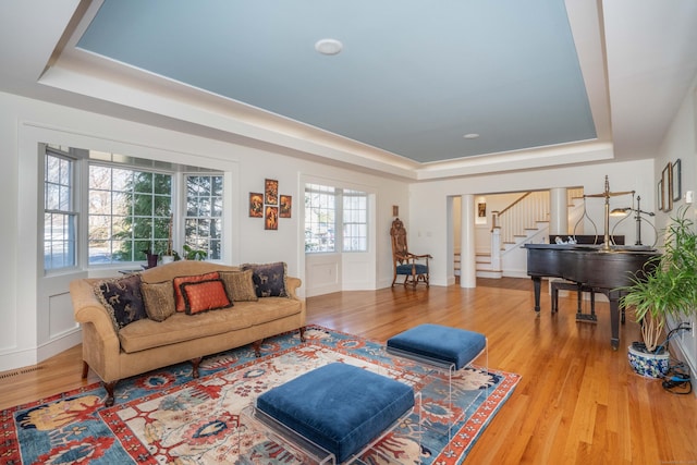 living room featuring a raised ceiling, stairway, wood finished floors, and visible vents