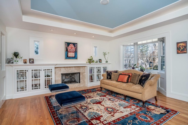 living room featuring a premium fireplace, a tray ceiling, and wood finished floors