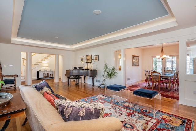 living room featuring a tray ceiling, an inviting chandelier, wood finished floors, and stairs