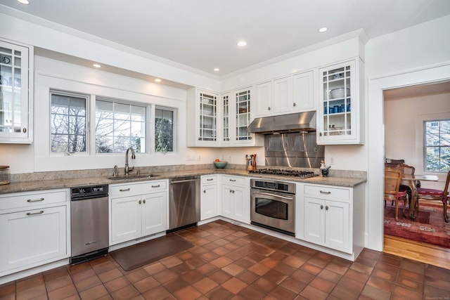 kitchen featuring light stone countertops, a sink, white cabinets, under cabinet range hood, and appliances with stainless steel finishes