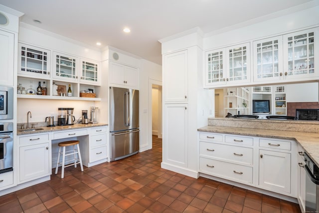 kitchen with appliances with stainless steel finishes, white cabinetry, glass insert cabinets, and a sink