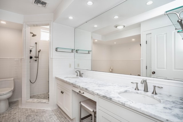 bathroom featuring toilet, tiled shower, visible vents, and a sink