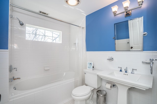 bathroom with visible vents, wainscoting, toilet, and tiled shower / bath