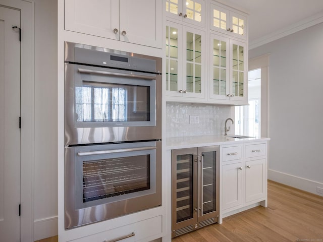 412 Tanner Marsh Rd, Guilford, CT 06437 - indoor wet bar featuring stainless steel double oven, wine cooler, backsplash, light wood-style flooring, and crown molding