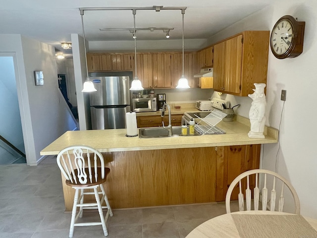 kitchen featuring brown cabinets, under cabinet range hood, stainless steel appliances, a peninsula, and light countertops