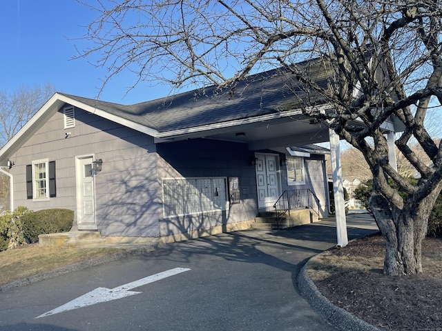 view of side of property featuring aphalt driveway, an attached carport, and a shingled roof