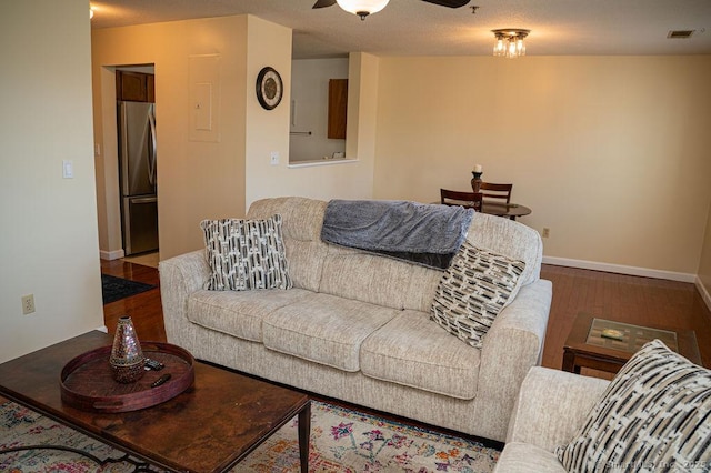 living area featuring visible vents, baseboards, a ceiling fan, and wood finished floors